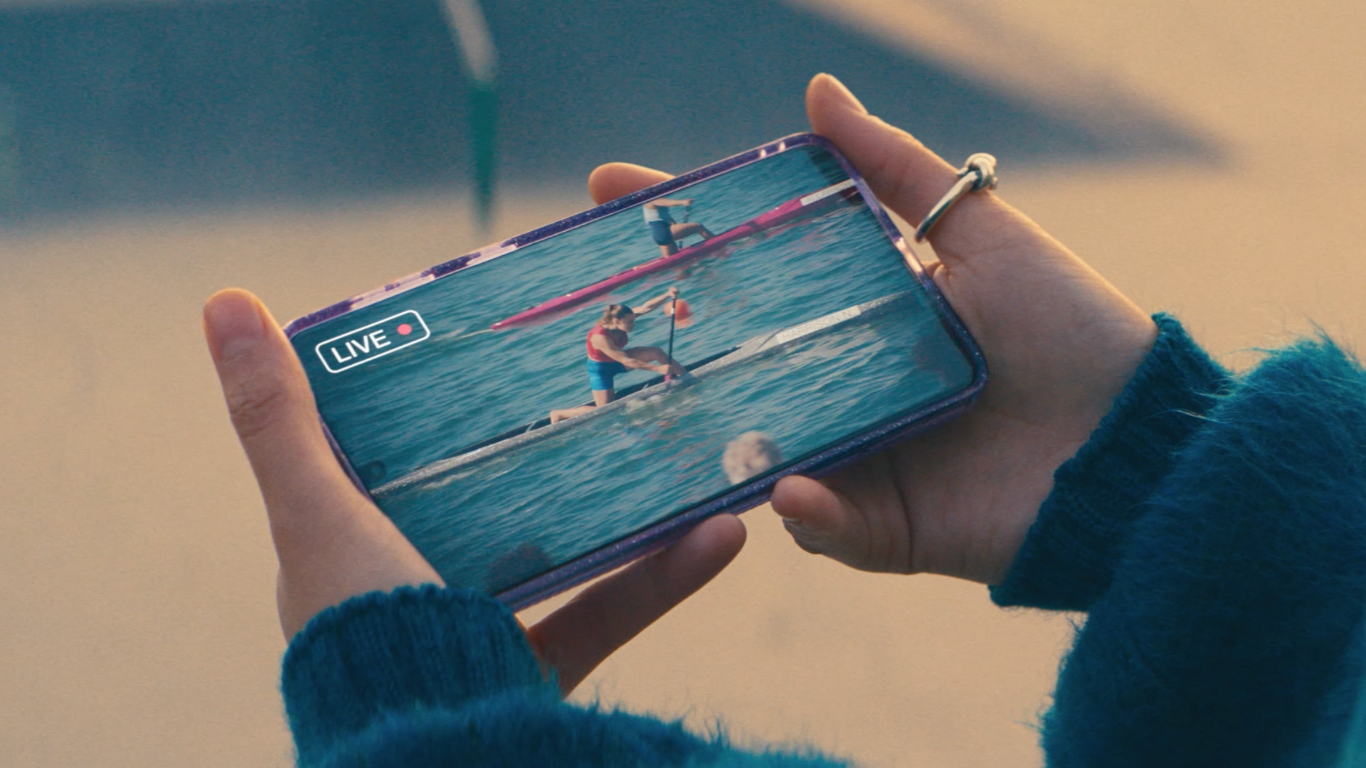 Person holding a phone and watching an athlete row across water live