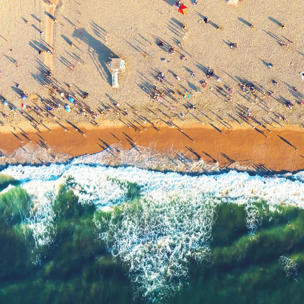 Vista aérea de una playa con sombrillas, y la arena y las olas en primer plano.