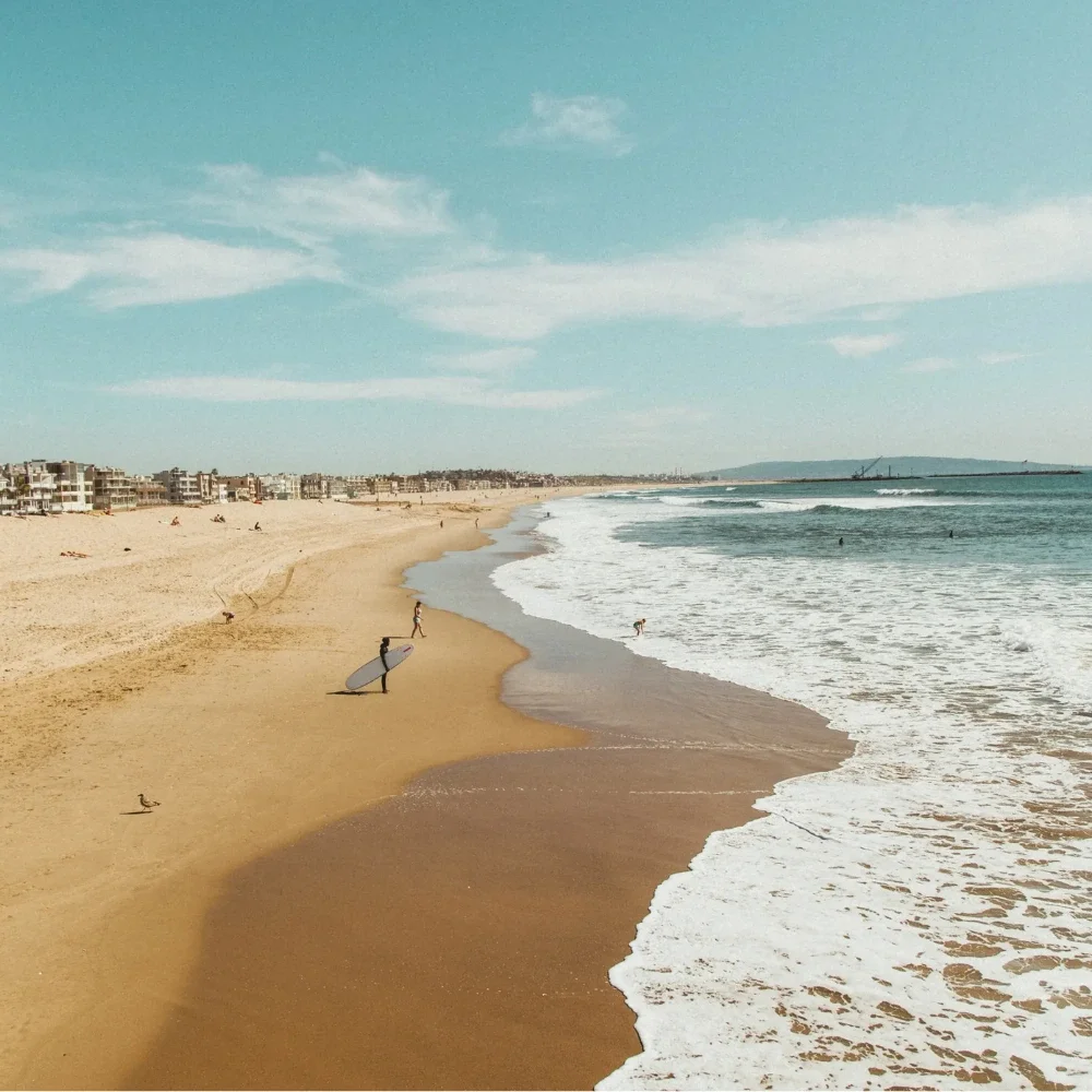Photo of an ocean shot in California with two surfers carrying their surfboards in the background