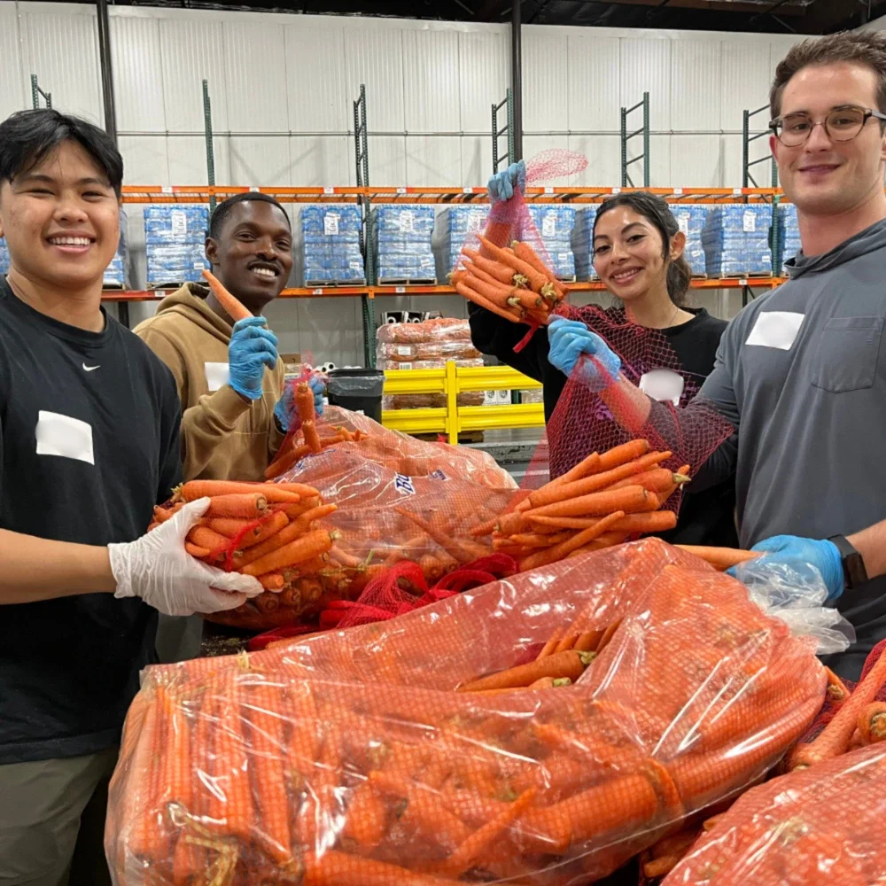 A group of people smiling and standing around a table of carrots that they are sorting
