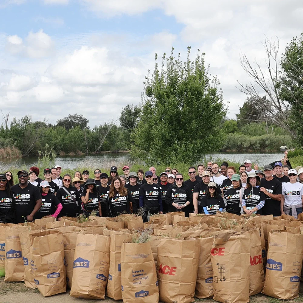 LA28 volunteers in black t-shirts standing in front of the Sepulveda Basin they helped clean up. Brown paper bags with vegetation inside is in the forefront.