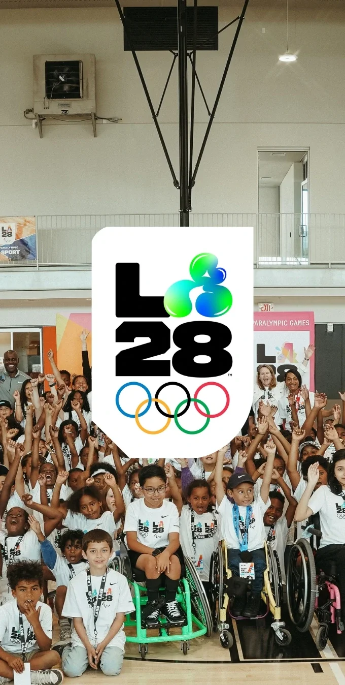 A group of children in a group photo with LA28 signage with the LA28 Youthful Energy emblem overlayed on top. 