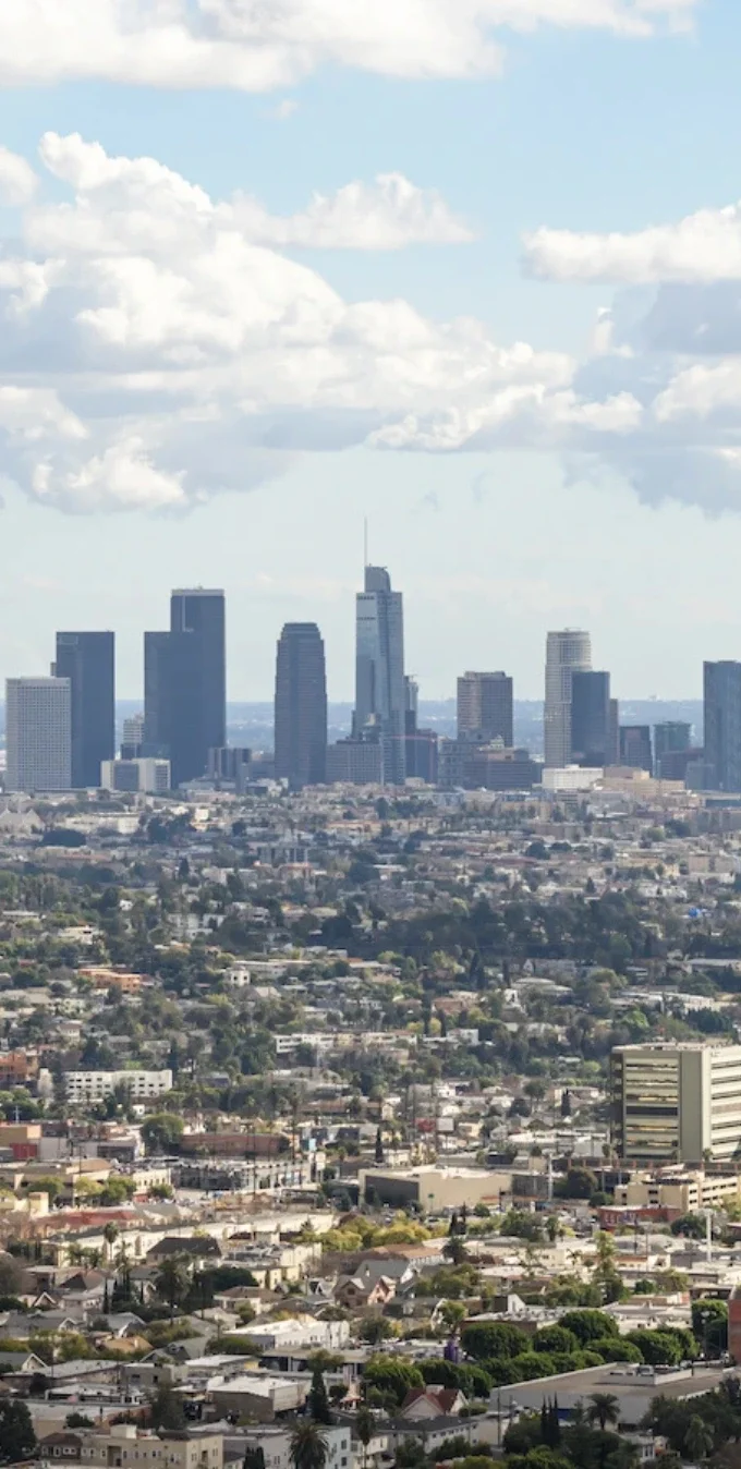 Los Angeles downtown skyling in the background with bright blue skies and clouds in front, with other LA neighborhoods in the foreground