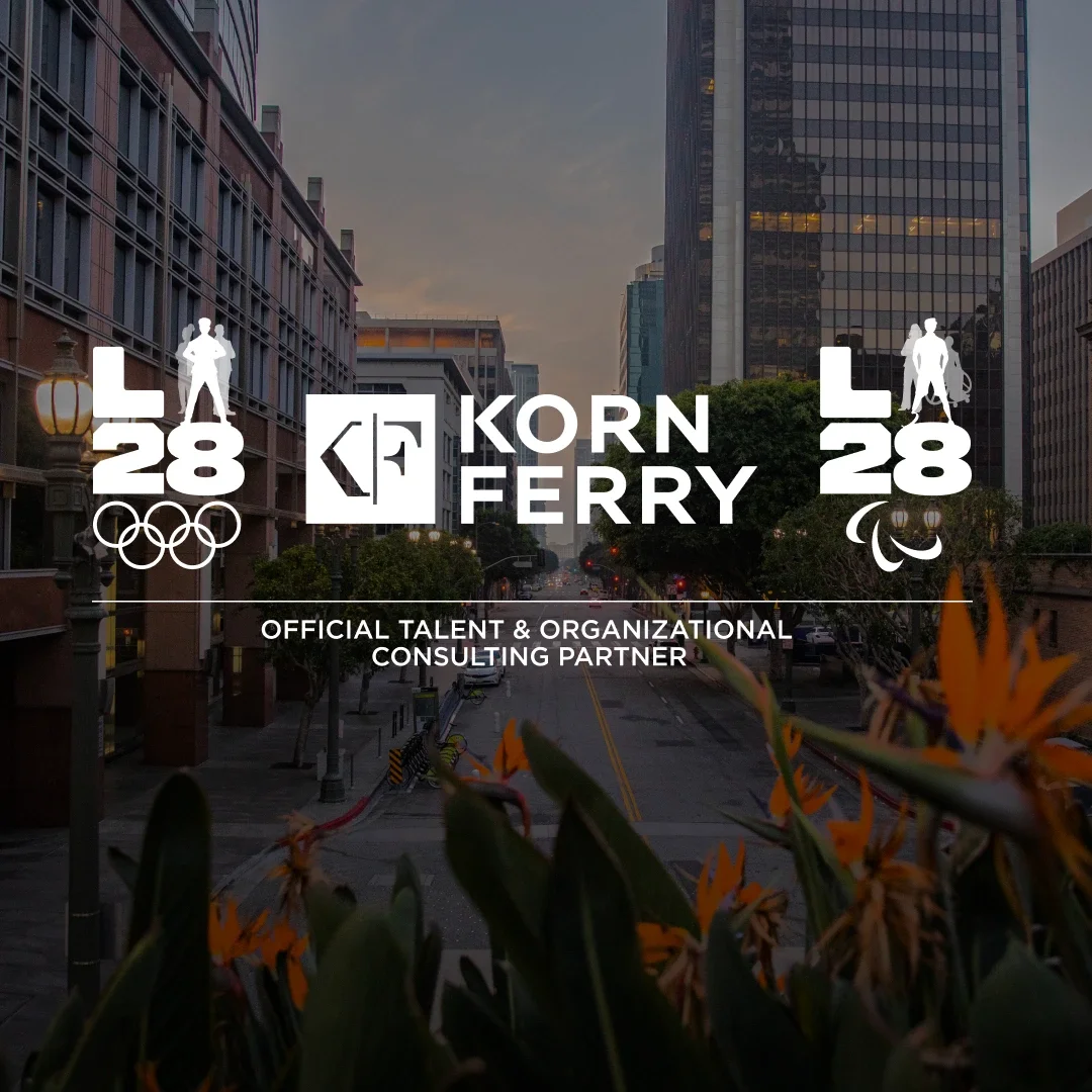 City scape background of Los Angeles with birds of paradise in the background and the Korn Ferry logo in white and the Korn Ferry LA28 Olympic and Paralympic A emblems on the sides with Founding Partner underneath