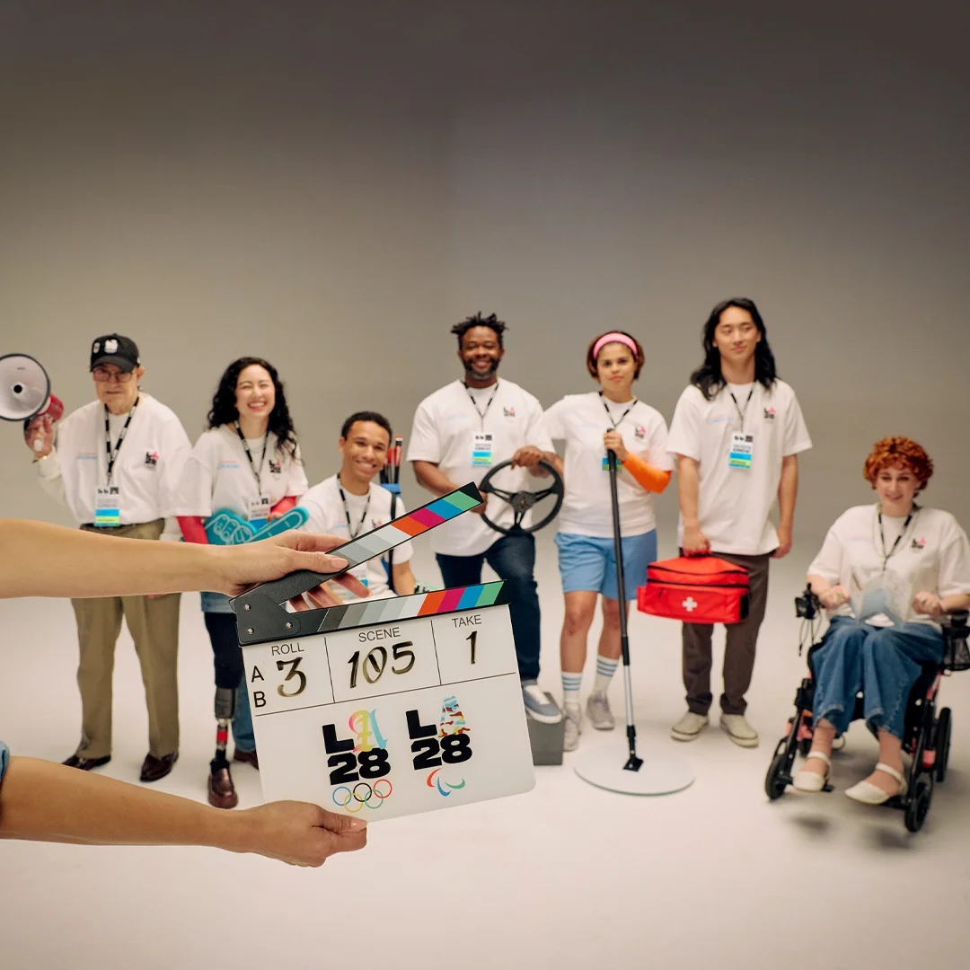 LA28 volunteers in white t-shirts in the background with a clapboard in the forefront with the numbers 3, 105 and 1 and the LA28 dual emblem on the clapboard.
