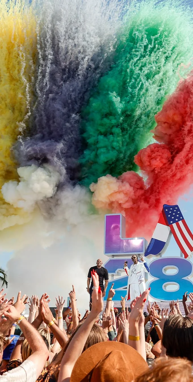 Photograph of the LA28 Handover Celebration stage in Long Beach with smoke in the Olympic ring colors rising in the background.