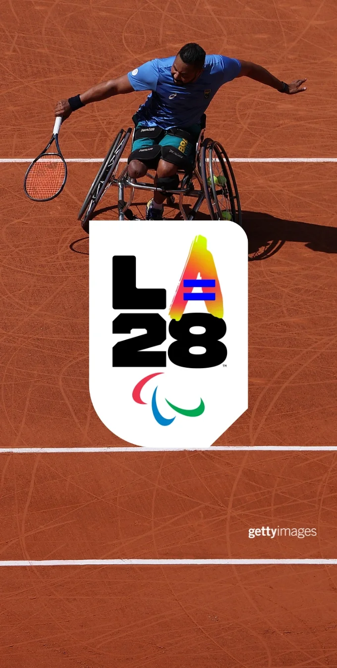 Una fotografía de un tenista paralímpico en silla de ruedas lanzando una pelota de tenis en una pista de tenis con el emblema personalizado de Igualdad de la 'A'  paralímpica de LA28.