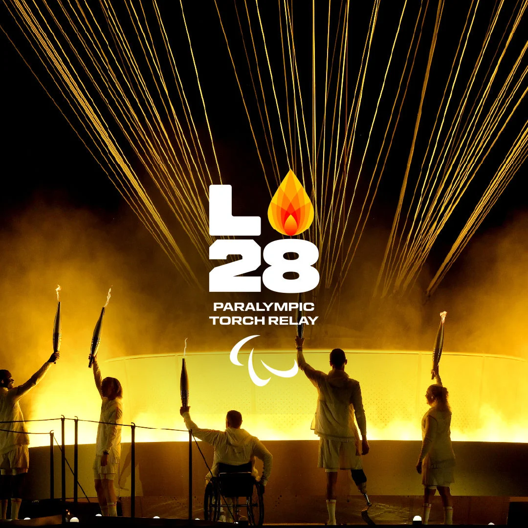Paralympic torch bearers on a stage with golden light in the background while raising their torches in the air