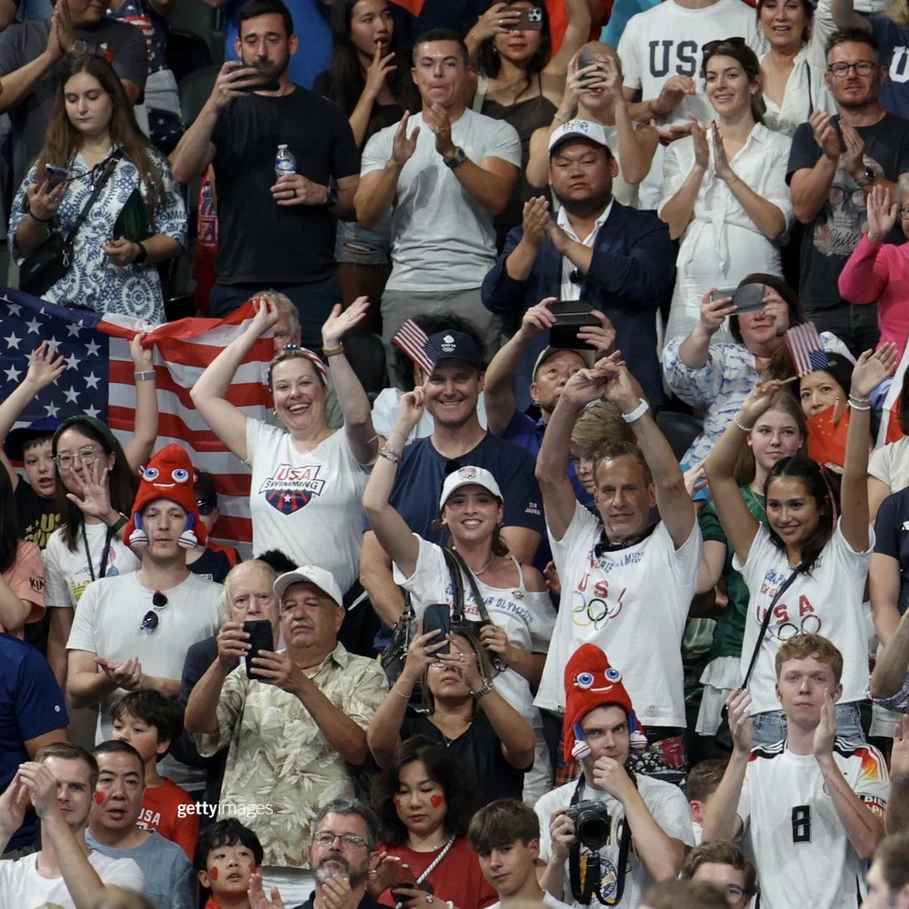 Fans cheering in the stands during the Olympic Games, many of them wearing Team USA gear.