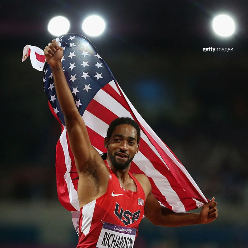 Photo of Jason Richardson holding the American flag in the air while wearing a red Team USA track uniform