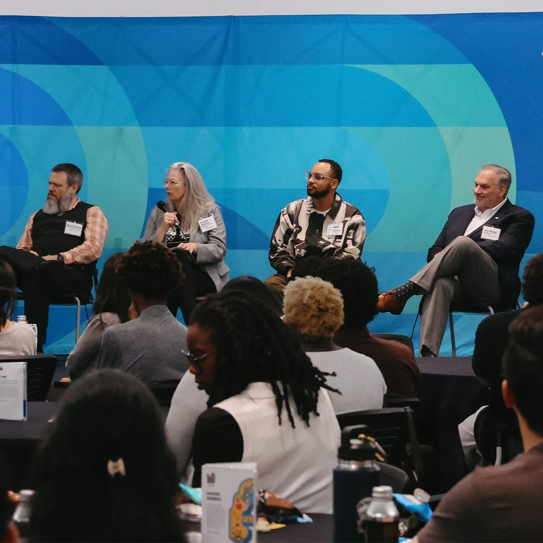 Group of panelists from LA28 sit in front of a bluebell bloom background while looking at the moderator speak.