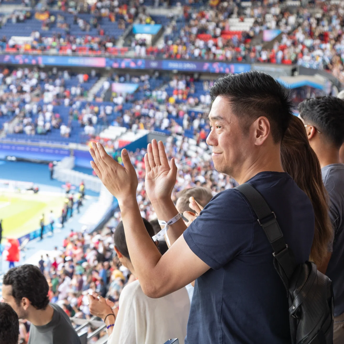 Un hombre con camisa azul marino aplaudiendo en su asiento en un estadio.