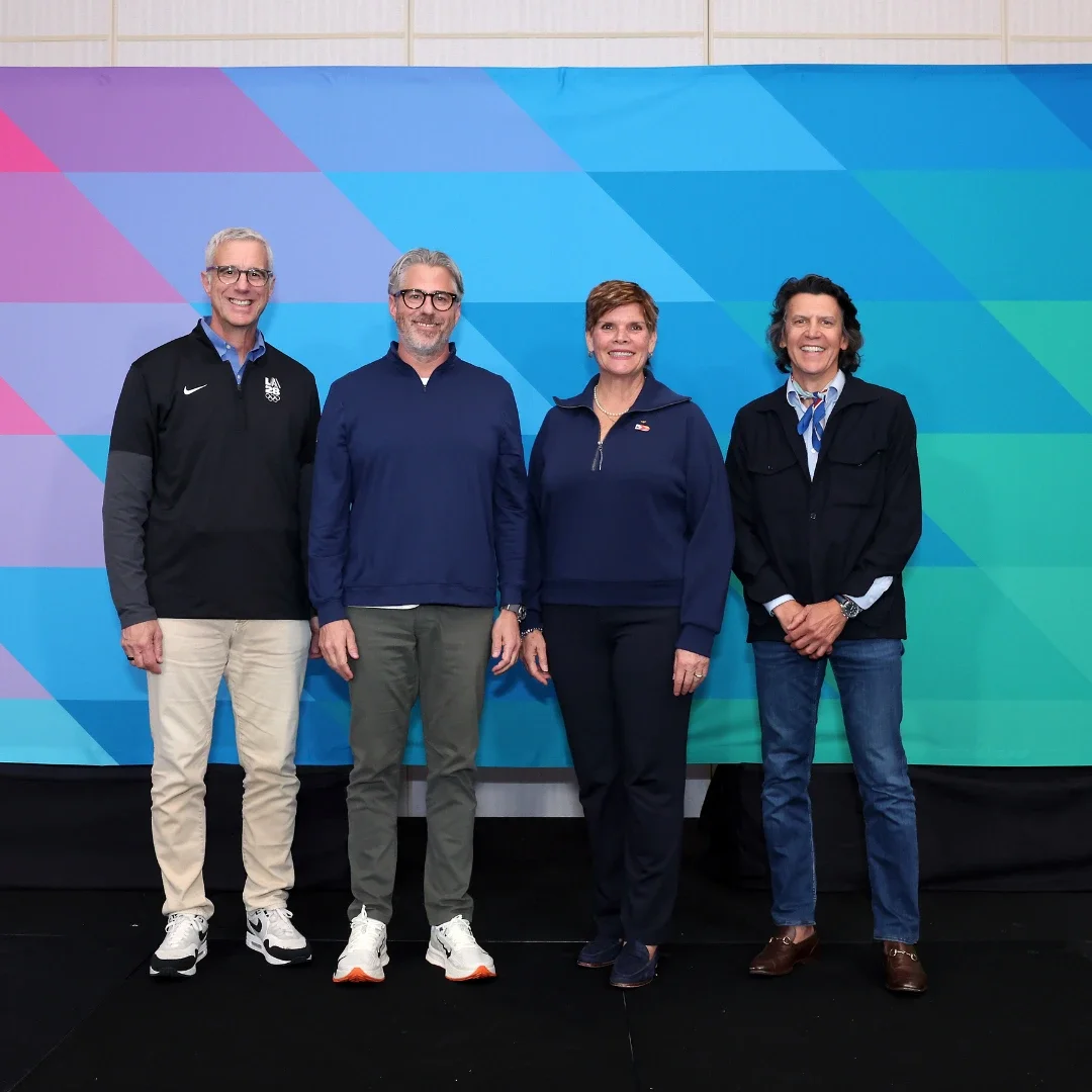 LA28 CEO Reynold Hoover, LA28 Chairperson Casey Wasserman and members of the International Olympic Committee standing together in front of a backdrop for the LA28 Games.