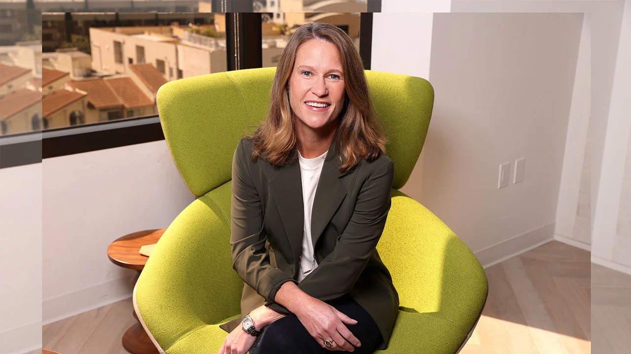 A photo of Kathy Carter sitting in a lime green chair smiling with her hands crossed across her lap wearing a gray blazer white shirt and black pants