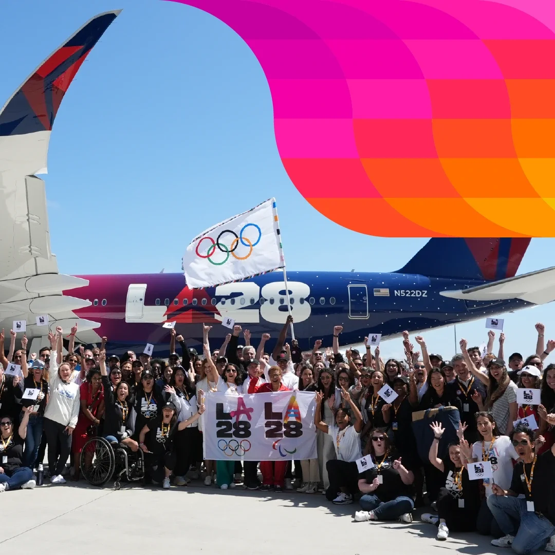 Fotografía mostrando el personal de LA28 sosteniendo la bandera de los anillos olímpicos y la bandera de LA28 en frente del avión de Delta del vuelo de la bandera olímpica