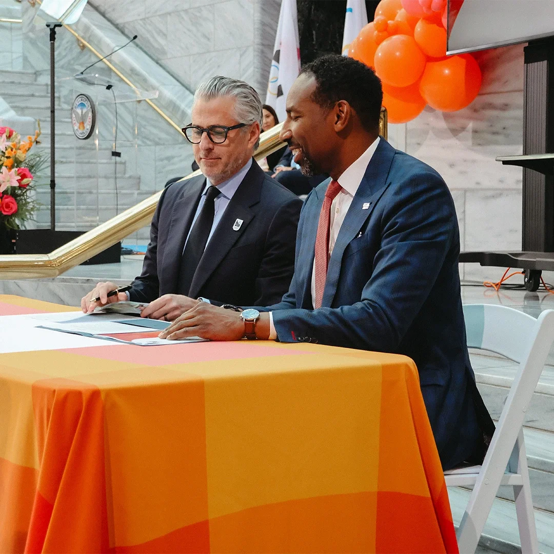 Casey Wasserman and Mayor Andre Dickens signing moment with orange balloons and flowers in the background