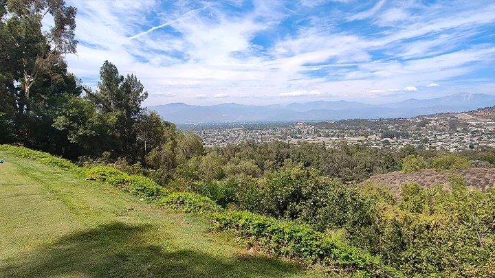A photograph of the Industry Hills MTB Course with grass in the foreground, and trees with the San Gabriel Mountains in the background