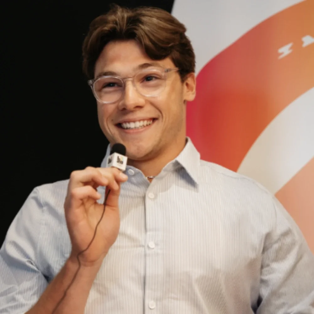 Paralympian Jack O'Neil smiling while sitting and holding a tiny mic with the LA28 emblem on it