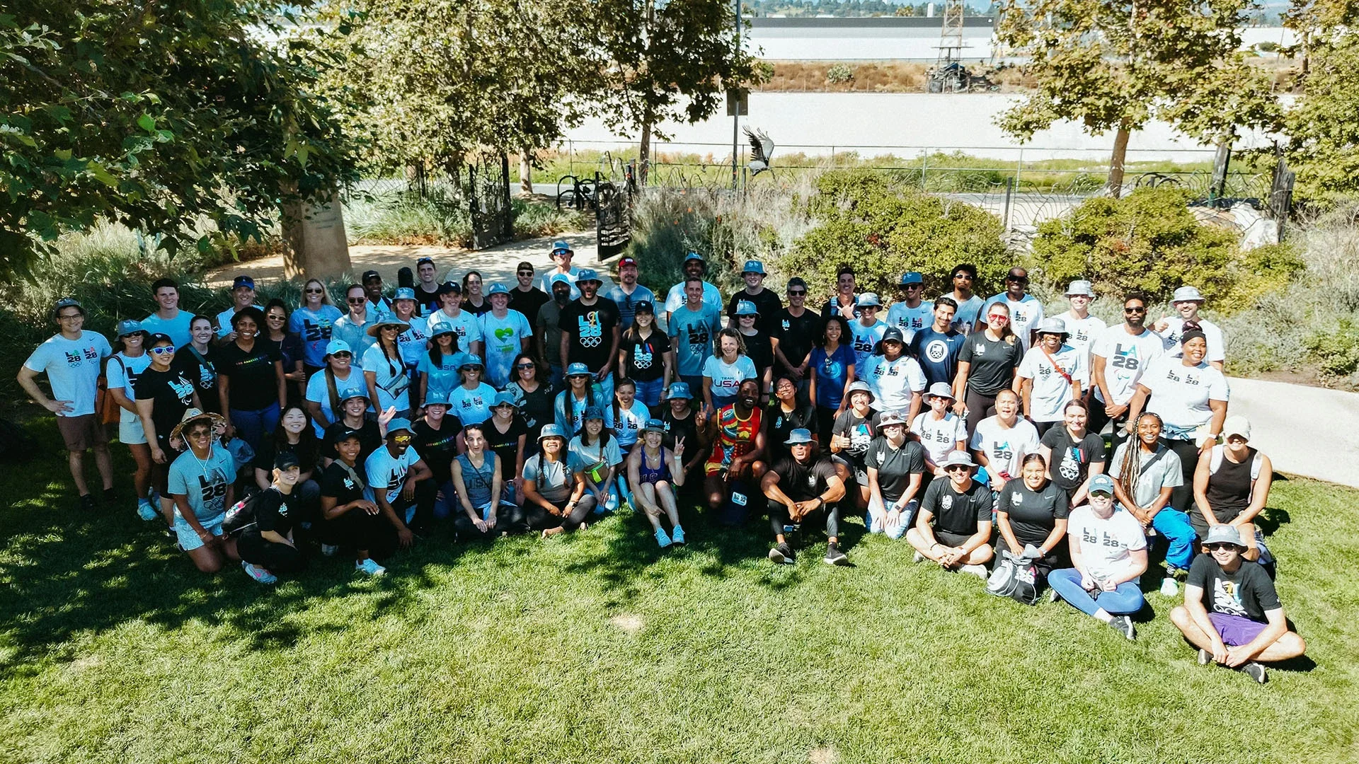 A group photo of many LA28 staff sitting on the grass smiling for a group photo in front of the LA river