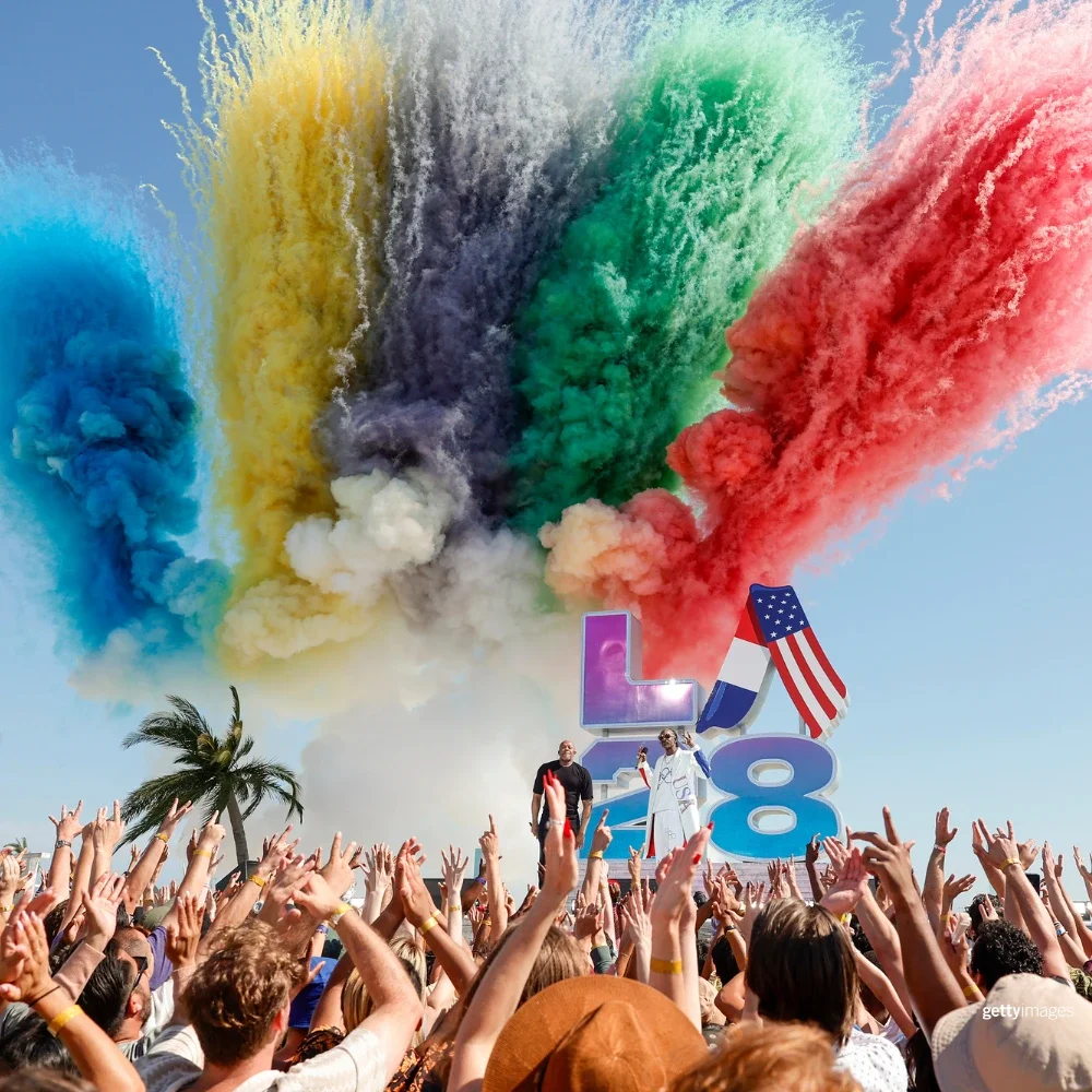 photo of colored smoke in black, blue, red, yellow and green in front of a stage withh Dr. Dre and Snoop Dogg singing at the LA28 Olympic Handover reveal ceremony