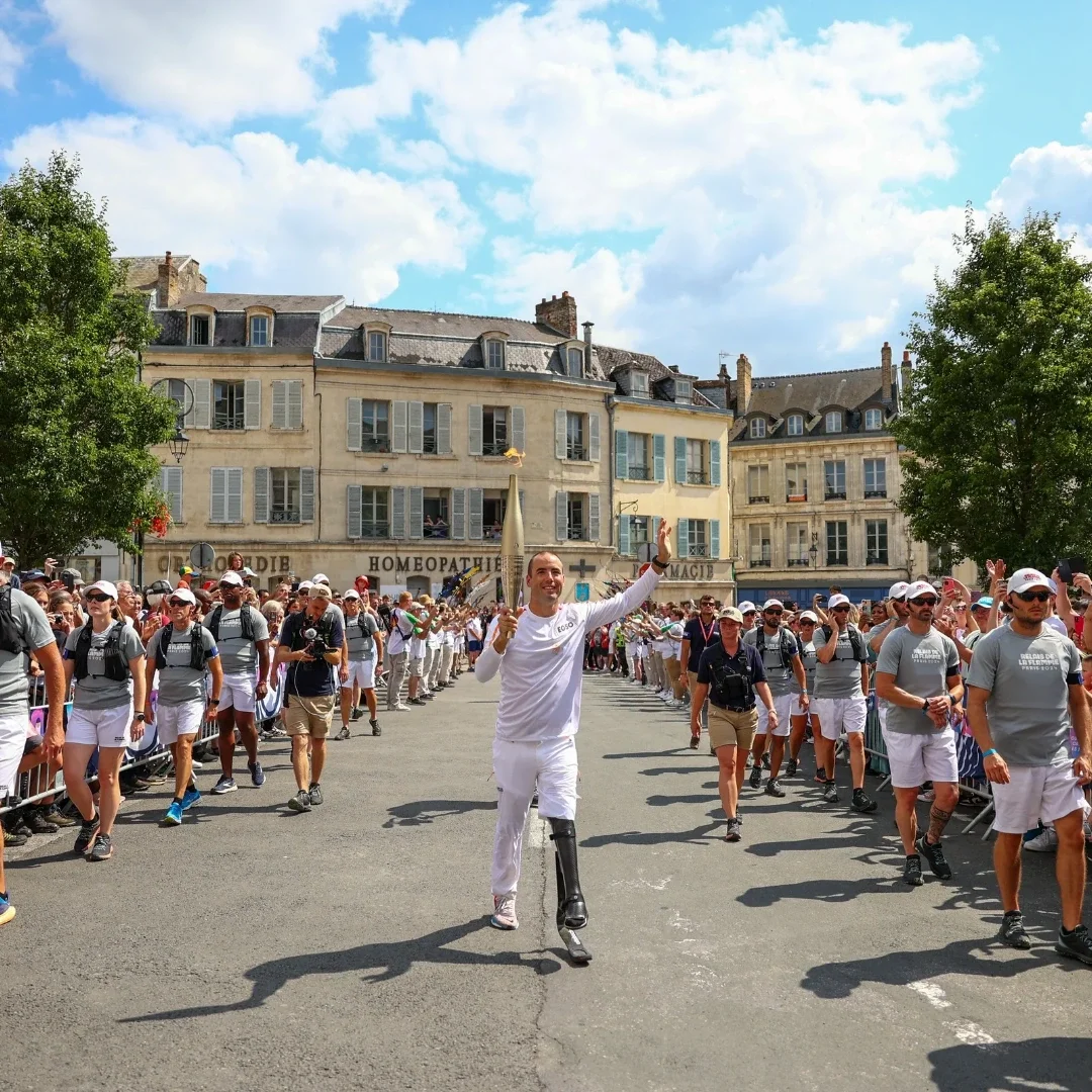An image of a runner carrying the Paralympic flame through the streets packed with fans.