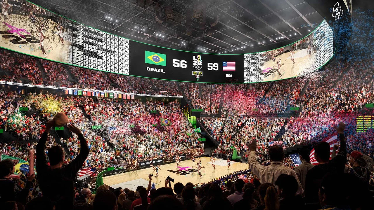 A digital rendering shows a busy basketball game at the Olympic and Paralympic Arena, also known as the Intuit Dome. The scoreboard shows USA 59 and Brazil 56, and the large digital screens surrounding the court display the game action. The stadium is full of excited fans waving flags from many countries. The court has the LA28 logo, indicating it's an Olympic game. There are many colorful lights and confetti on the scene.