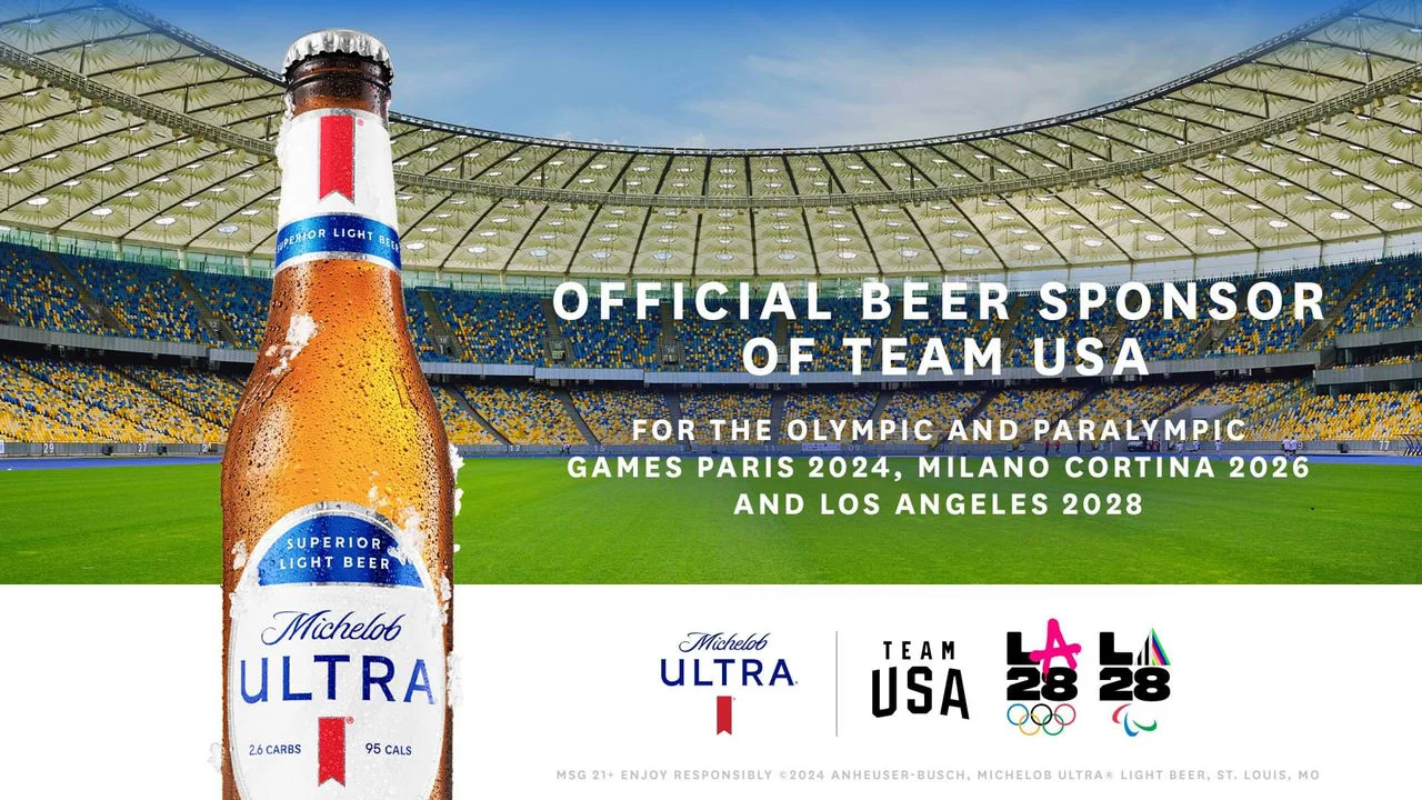 Imagen que muestra el interior de un estadio, con una botella de cerveza Michelob Ultra y las palabras "Cerveza oficial de Team USA para los Juegos Olímpicos y Paralímpicos de París 2024, Milano Cortina 2026 y Los Ángeles 2028".