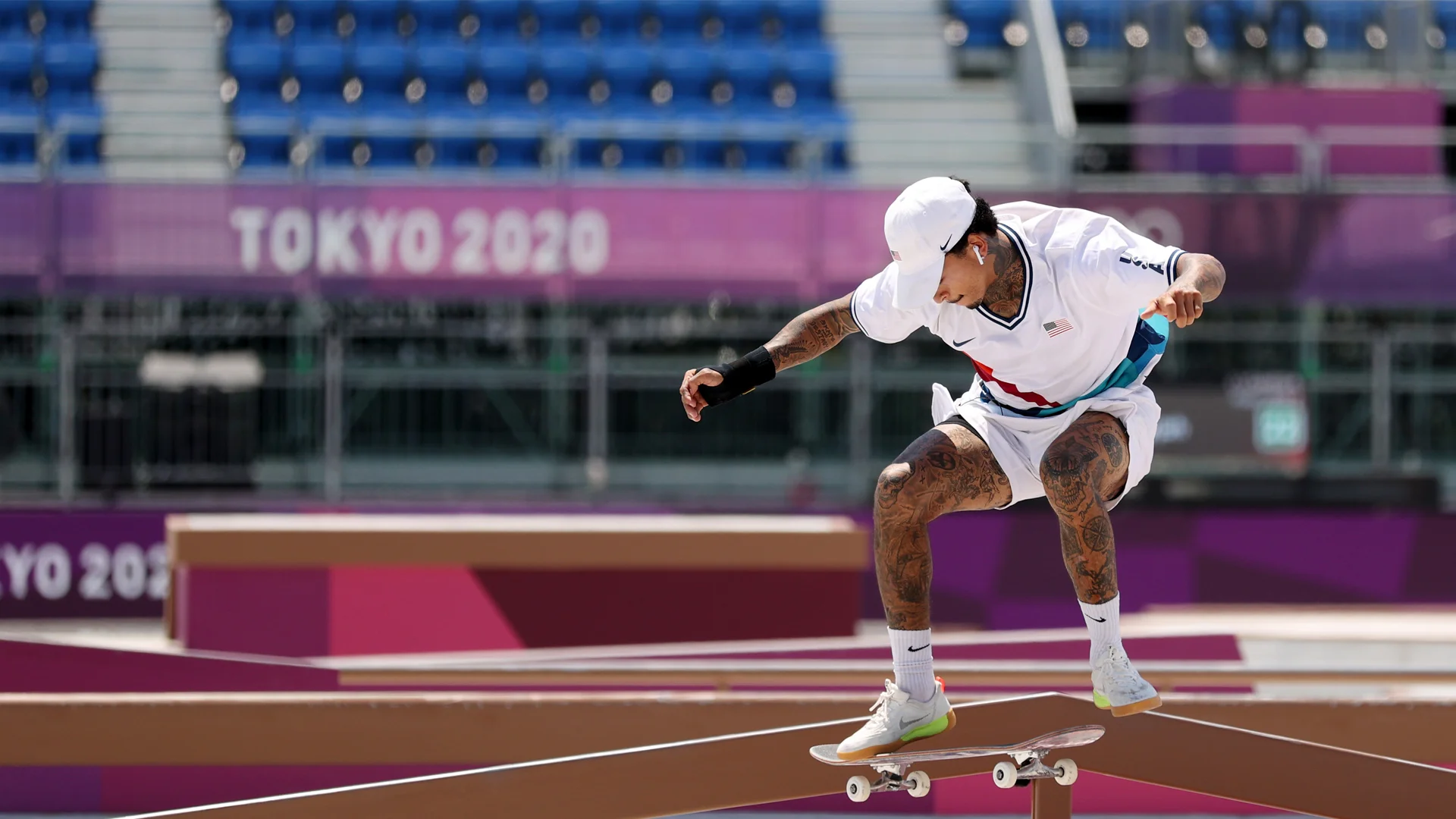 A skateboarder jumping onto his skateboard in white shorts, shirt, hat, socks and shoes