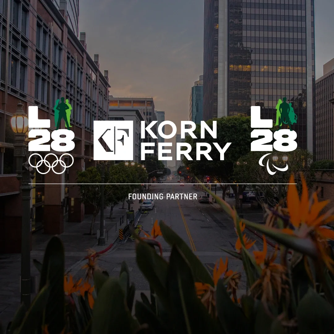 City scape background of Los Angeles with birds of paradise in the background and the Korn Ferry logo in white and the Korn Ferry LA28 Olympic and Paralympic A emblems on the sides with Founding Partner underneath