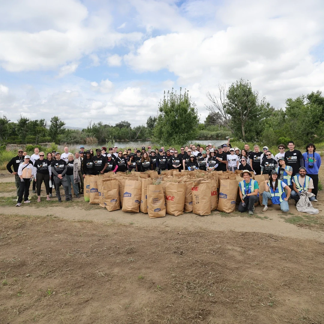 Group of LA28 volunteers in front of a landscape of hills and wildflowers with bags at the Sepulveda Basin in Los Angeles