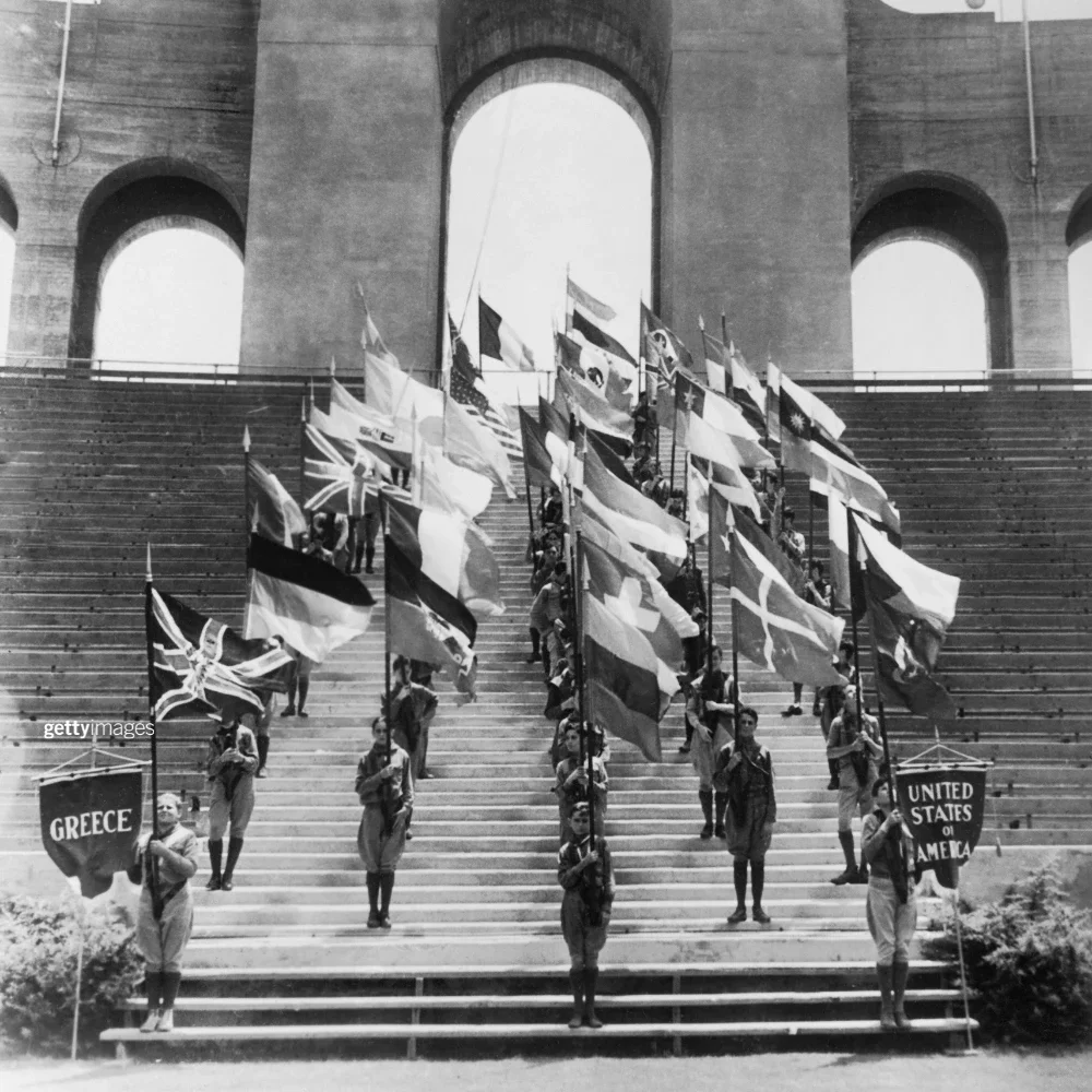 Black and white photo showcasing representatives from several countries holding their home flags on the steps of the LA Memorial Coliseum during the 1932 Games