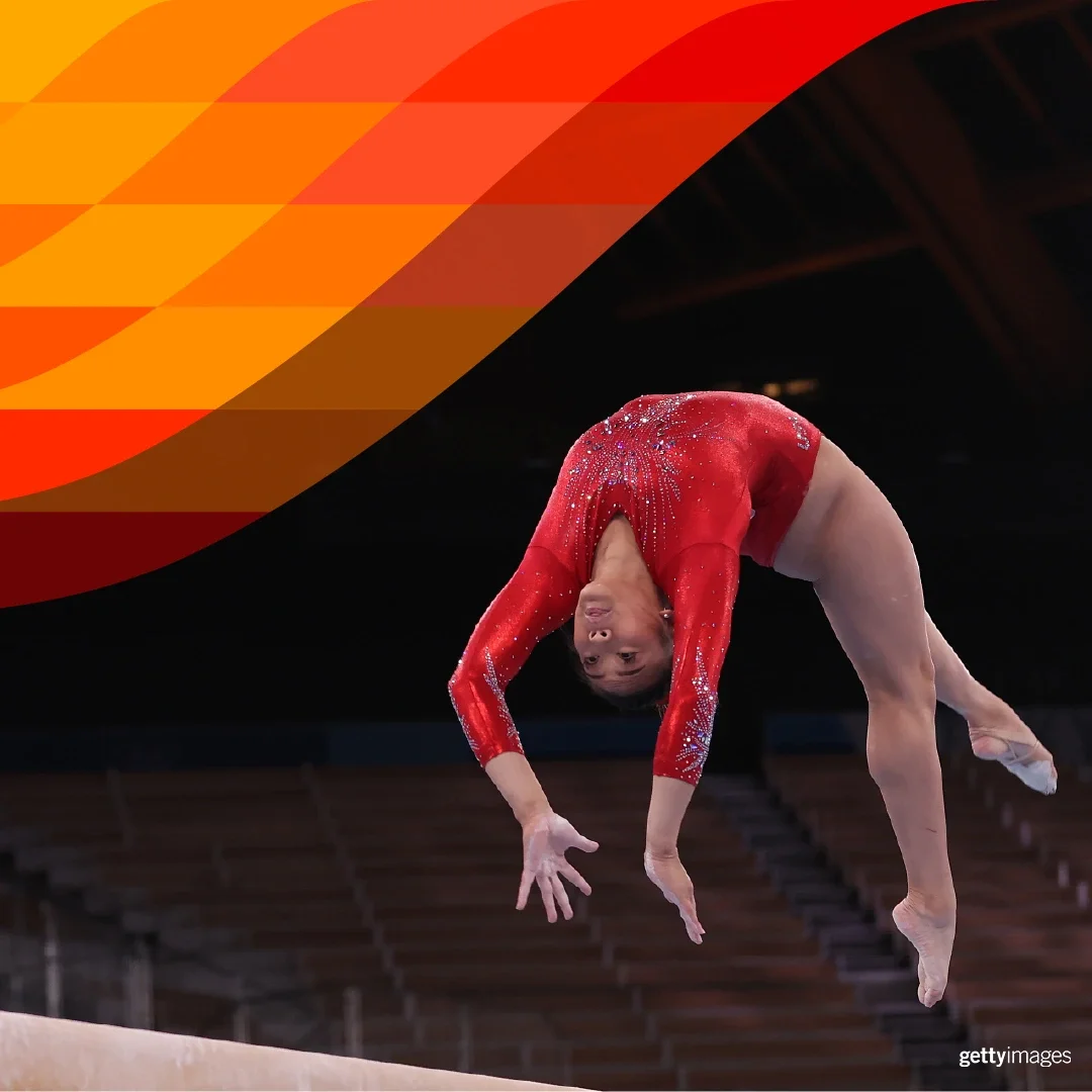photograph of a female gymnast in a red leotard doing a back flip on a beam caught in mid air