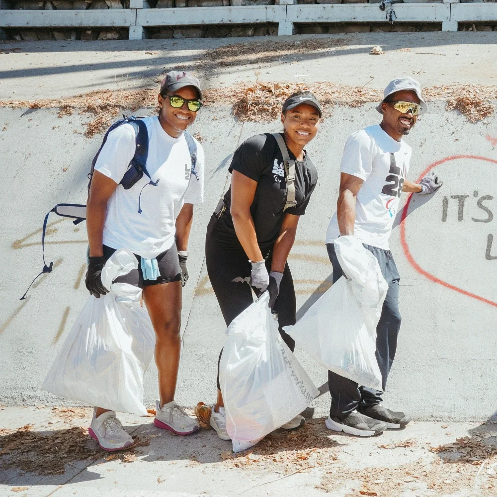 A photograph of two women and one male standing next to each other smiling while holding trash bags