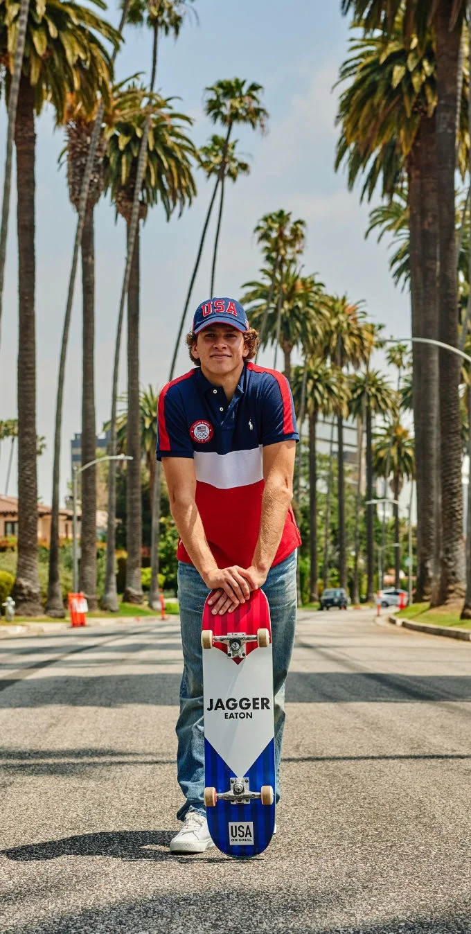 El patinador Jagger Eaton de pie con una patineta de Team USA en frente de una calle residencial en Los Ángeles. 